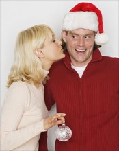 Woman kissing man in Santa hat.
