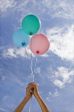 Hands holding balloons toward sky.