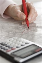 Woman checking financial page with calculator.
