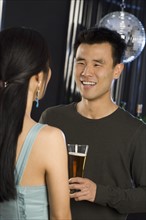 Man with beer talking to woman in nightclub.