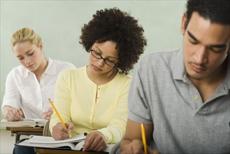 Three college students in class taking test.