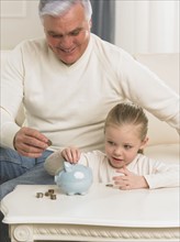 Grandfather and young granddaughter putting change in piggy bank.
