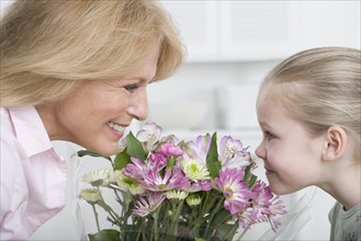 Grandmother and young granddaughter smelling bouquet of flowers.