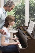 Woman playing piano with man watching.
