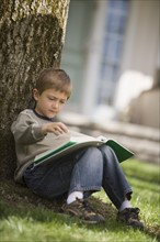 Young boy reading under a tree.