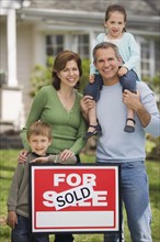 Family in front of house with For Sale/Sold sign.