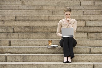 Young woman sitting outdoors on stairs with laptop.