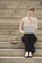 Young woman sitting outdoors on stairs with laptop.