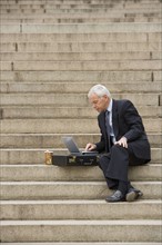 Man sitting outdoors on stairs with laptop.