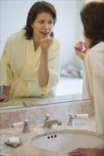 Woman putting on lipstick in bathroom.