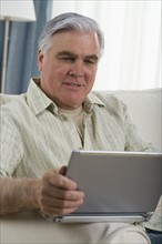 Senior man using laptop on sofa.
