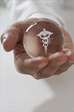 Close up of man holding clear ball with Caduceus symbol.