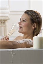 Woman in bathtub drinking champagne.