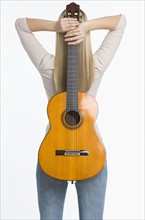 Studio shot of woman holding guitar against her back.