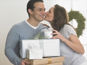 Woman kissing man holding Christmas gifts.