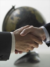 Two men shaking hands with globe in background.