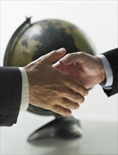 Two men shaking hands with globe in background.