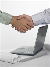 Two men shaking hands over laptop computer.