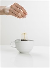 Studio shot of tea cup with woman's hand holding tea bag.