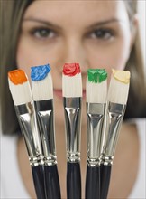 Paintbrushes with paint in front of woman's face.