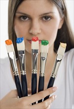 Paintbrushes with paint in front of woman's face.