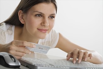 Woman holding credit card and using computer keyboard.