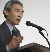 Senior Asian businessman speaking at podium.
