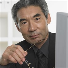 Senior Asian businessman holding eyeglasses.