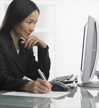Asian businesswoman looking at computer and writing.