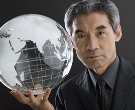 Senior Asian businessman holding clear globe.