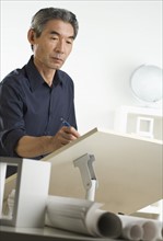 Asian businessman at drafting table with blueprints.