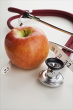 Close up of apple, tape measure and stethoscope.