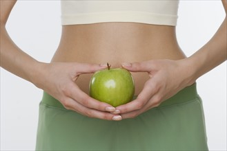 Studio shot of woman holding apple in front of belly.