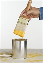 Close up of man dipping paintbrush in paint can.