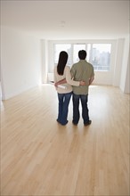 Rear view of couple with blueprints in empty room.