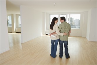 Rear view of couple with blueprints in empty house.