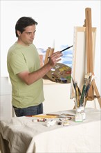 Man painting at easel indoors.