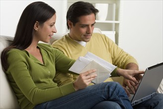 Couple with bills and laptop on sofa.