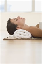 Woman laying on mat with rolled towel under neck.