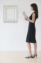 Woman in evening dress next to empty picture frame.