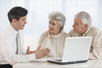 Businessman talking to senior couple in home.