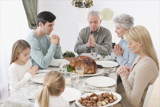 Family saying grace at Thanksgiving table.