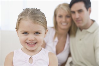 Girl smiling with parents in background.