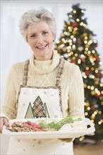 Senior woman holding tray of Christmas cookies.