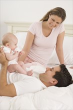 Parents playing with baby in bed.