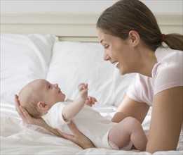 Mother smiling at baby on bed.