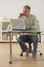 Senior man with bare feet looking at laptop.