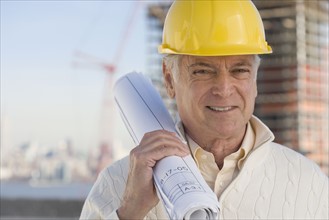 Senior man wearing hard hat and holding blueprints.