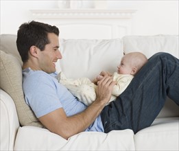 Father smiling at baby on sofa.