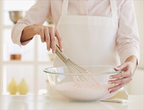 Woman wearing apron and mixing batter .